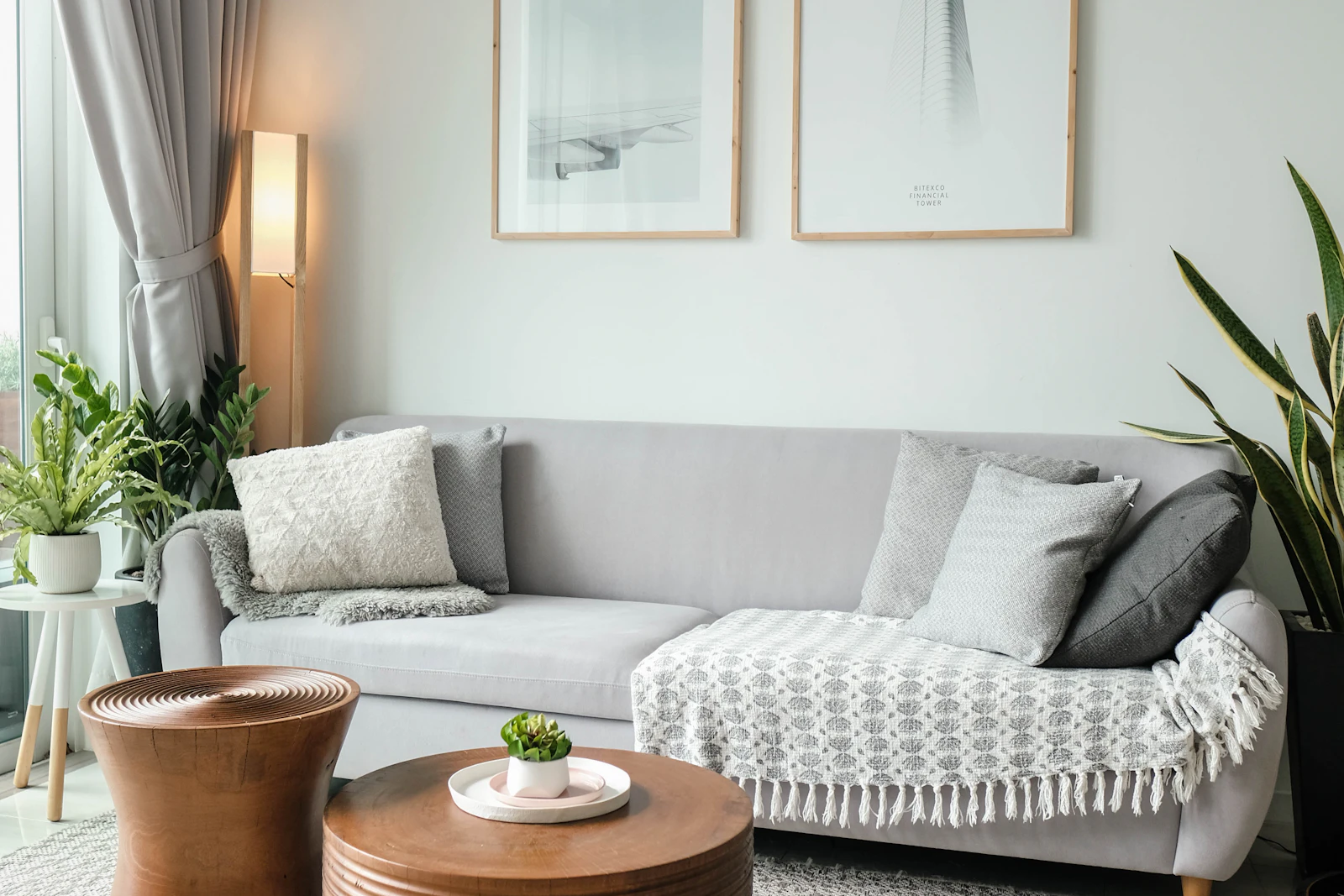 Gray sofa with wood side tables, plants, and two framed prints, shown as a furniture grouping example.