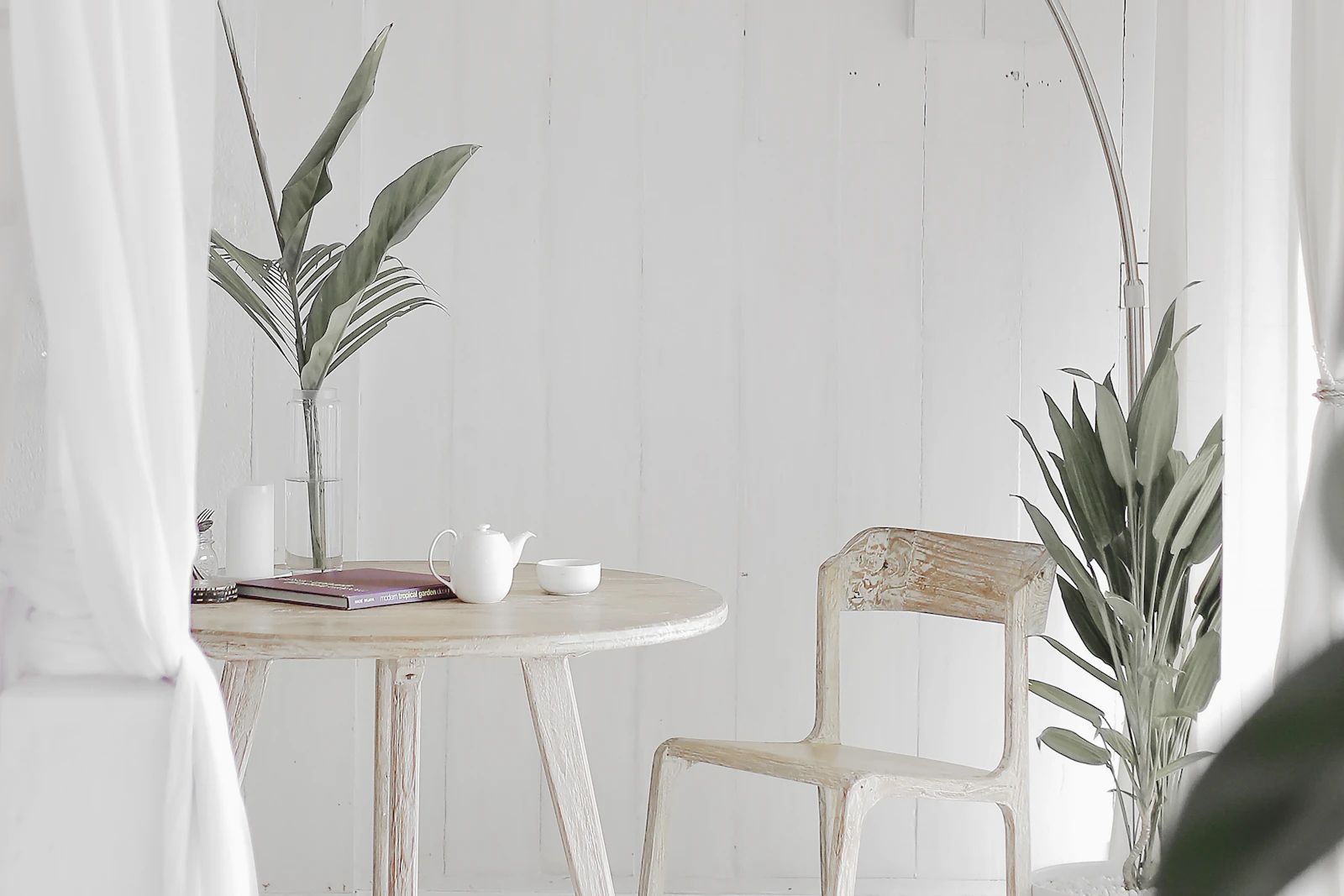Bright residential corner with a round wood table, teapot, book, plants, and a pale chair, shown as decorative styling inspiration.